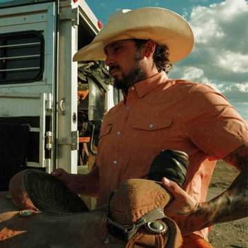 Man wearing The Joshua Tree shirt holding a saddle outdoors