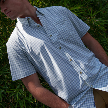 The Kawakawa blue checked short sleeve shirt worn outdoors in dappled sunlight