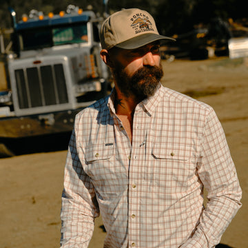 The Long Nose Pete maroon aqua white plaid men's outdoor shirt with long sleeves and chest pockets by a truck