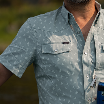 Close-up of a green patterned short sleeve shirt called The Lupine with a buttoned chest pocket and outdoor lanyard accessories