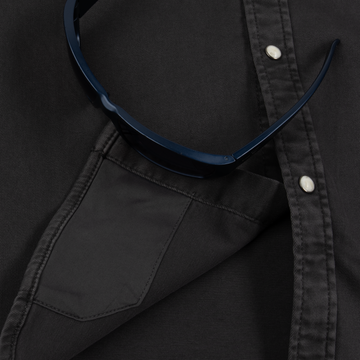 Close-up of a black button-up shirt pocket with sunglasses resting on The Matamoros shirt fabric.