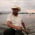 Man wearing The Medicine Bow shirt and cowboy hat paddling a canoe on a lake