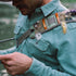 Close-up of a man wearing The Mentone shirt outdoors, focused on fly fishing near a river.