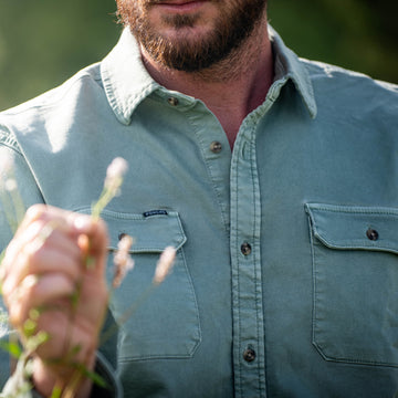 The Mentone green button up shirt worn outdoors by a bearded man holding wildflowers