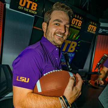 Man in a purple shirt holding a football inside a sports radio studio