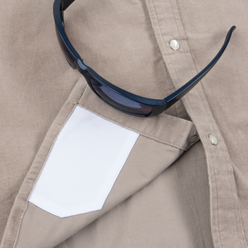 Close-up of The Mouflon shirt pocket holding a pair of black sunglasses on beige fabric background