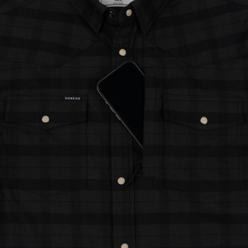 Close-up of a black checkered The North Rim shirt with snap buttons and a smartphone tucked into the chest pocket.