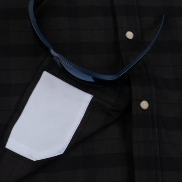 Close-up of a dark plaid shirt with white pocket detail and sunglasses resting on it, featuring The North Rim design.