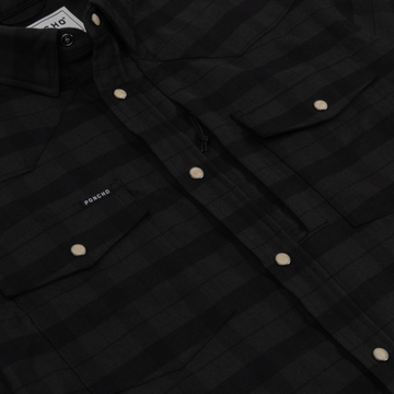 Close-up of The North Rim shirt in black check pattern with snap buttons and chest pockets showcasing a sleek outdoors style.