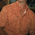 Close-up of a person wearing The Occupy Left Field shirt with an intricate yellow floral pattern on rust background outdoors style.