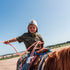Young boy wearing The Palomita shirt while riding a horse outdoors under a clear blue sky