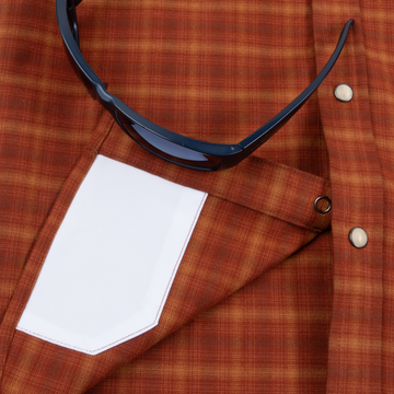 Close-up of The Pitstop shirt fabric in orange plaid with a white pocket and black sunglasses resting on it
