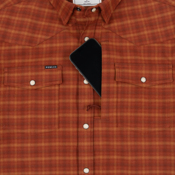 Close-up of The Pitstop shirt in orange plaid with snap buttons and a phone partially tucked into the chest pocket
