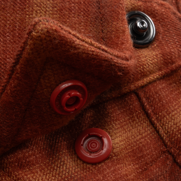 Close-up of rust-colored fabric with red and black buttons from The Pitstop shirt.