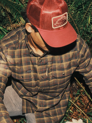 The Rusty Saw black, red, and tan plaid men's outdoor shirt with chest pockets in a forest