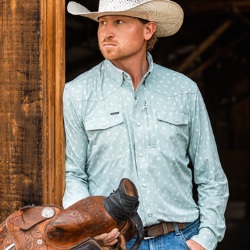 Man wearing The St. Helens shirt in light blue with subtle pattern, holding a leather saddle and wearing a cowboy hat.