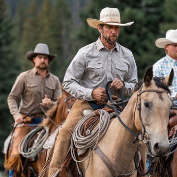 Man wearing The Stockton shirt and cowboy hat riding a horse outdoors with other riders in the background