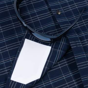 Close-up of The Sturgeon shirt pocket with sunglasses resting on navy plaid fabric