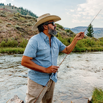 man with fishing rod by river wearing tip of the hat short sleeve pearl snap shirt