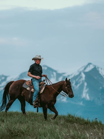 Man wearing The Bandera shirt riding horse outdoors with mountain backdrop