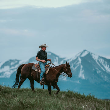 Man wearing The Bandera shirt riding horse outdoors with mountain backdrop