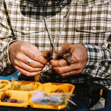 Man sitting down tying on streamer fly in The Boone Shirt
