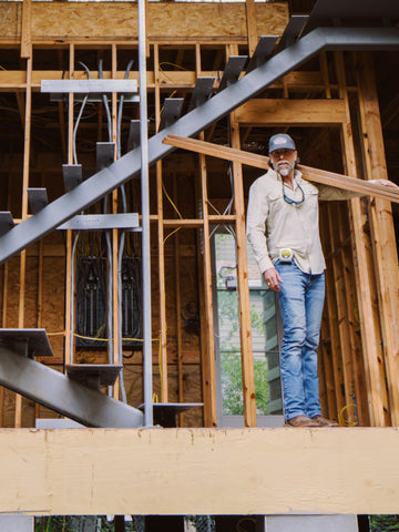 Man wearing The Brush Buster shirt standing on construction site carrying wooden planks