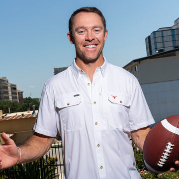 Smiling man in a white button-down shirt holding a football outdoors against a city skyline