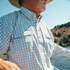 The Soda Butte plaid shirt worn outdoors by a man near a scenic river and wooded hills
