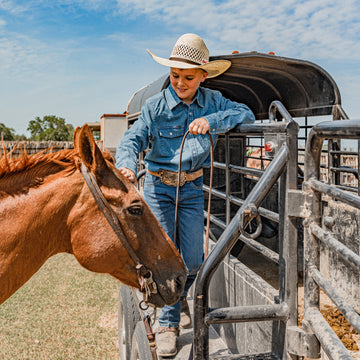 Young cowboy petting his horse wearing dark denim