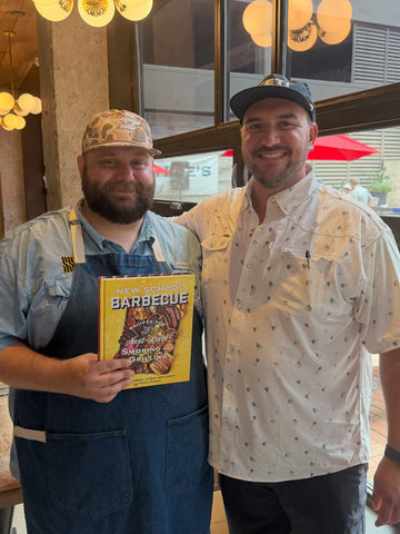 Two smiling men wearing shirts pose indoors, with one holding a New School Barbecue magazine