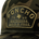Close-up of a camouflage hat featuring an embroidered patch that reads "Poncho TX US Outdoors Wild & Free" with a Texas silhouette.