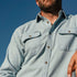 Man wearing a light blue men's outdoor shirt with buttoned chest pockets under a clear blue sky
