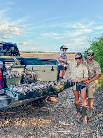 Three anglers beside a pickup truck loaded with fish in a sunny marshland setting