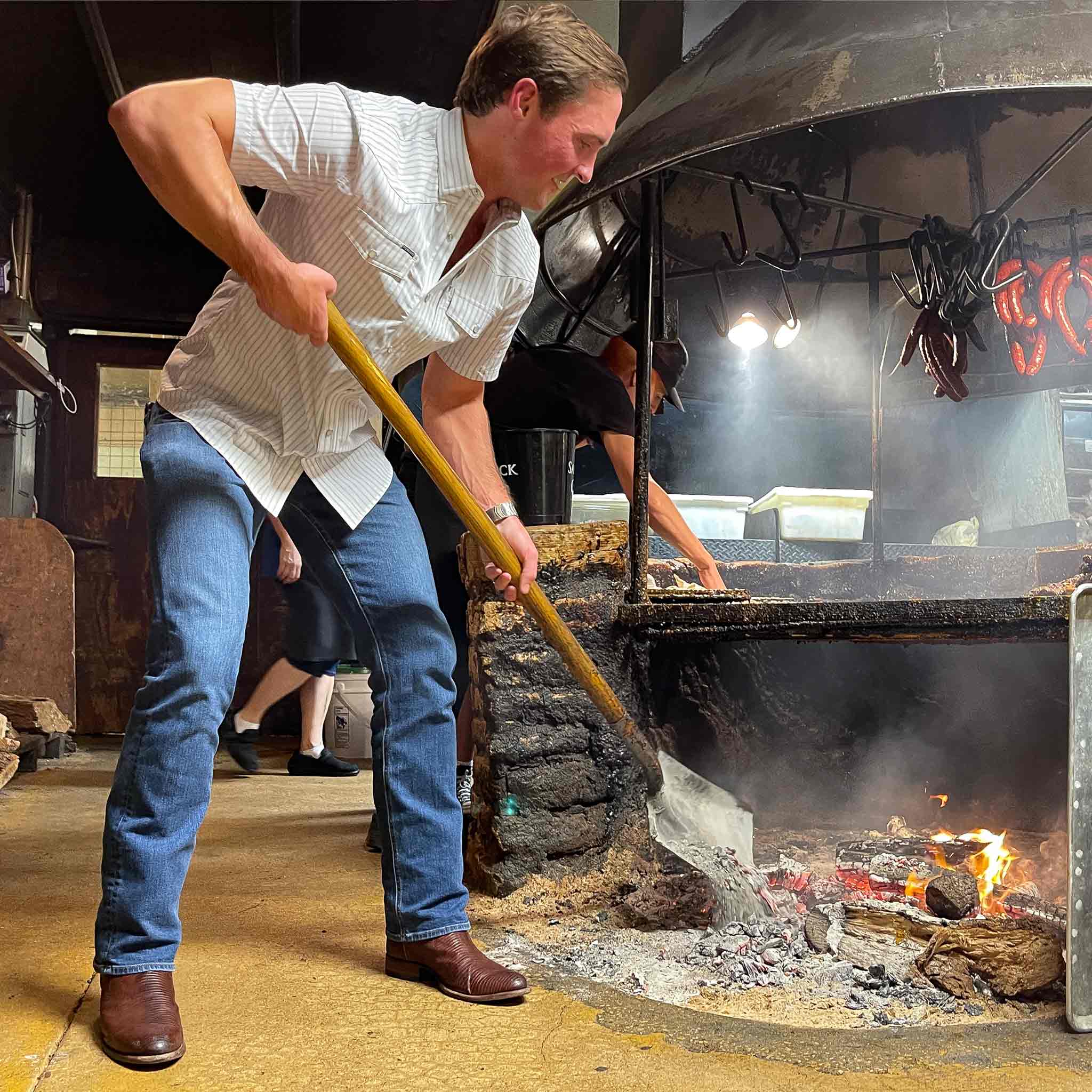 Photo of man shoveling wood into a fire pit wearing striped shirt