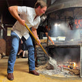 Photo of man shoveling wood into a fire pit wearing striped shirt