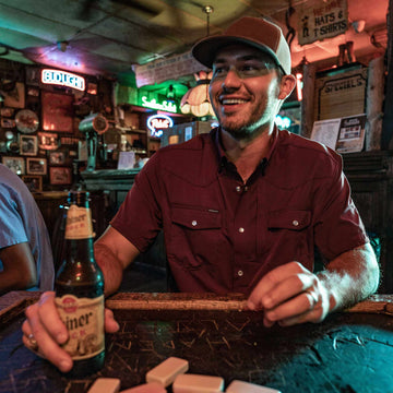 man wearing maroon short sleeve pearl snap shirt with beverage