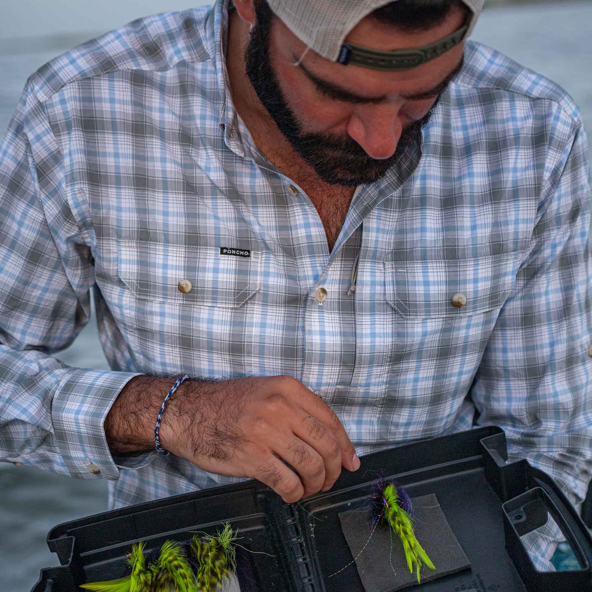 man tying fly while wearing grey / blue plaid long sleeve shirt