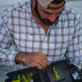 man tying fly while wearing grey / blue plaid long sleeve shirt