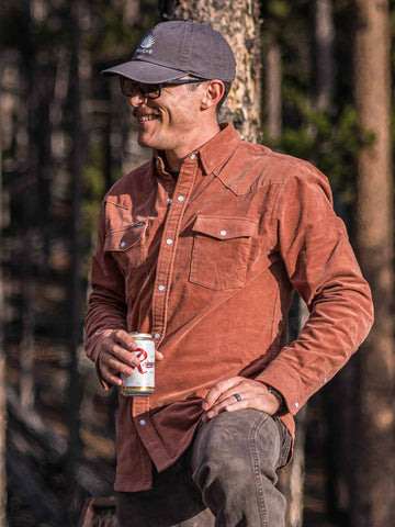 guy wearing shirt standing in woods holding beer