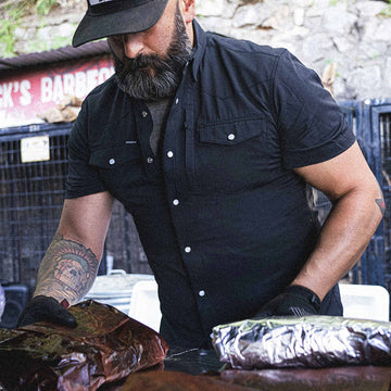 Man wearing black short sleeve shirt wrapping brisket