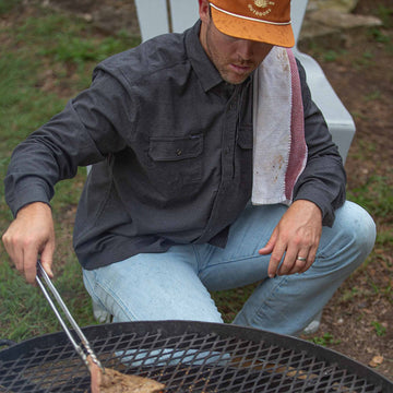 Man wearing dark grey flannel cooking steaks on grill
