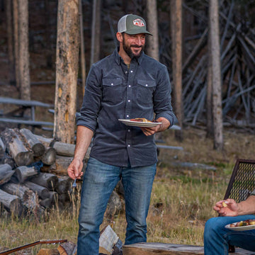 guy wearing navy corduroy pearl snap shirt holding food near campfire