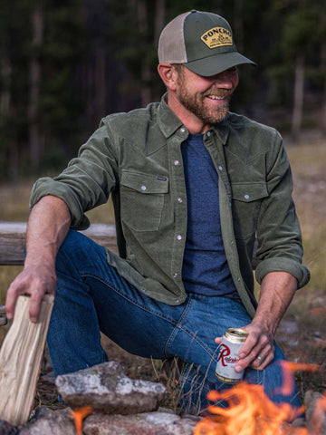 guy wearing olive green corduroy shirt sitting in front of campfire
