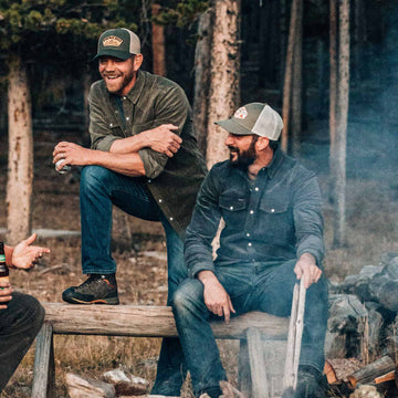 two guys wearing corduroy shirts sitting around fire