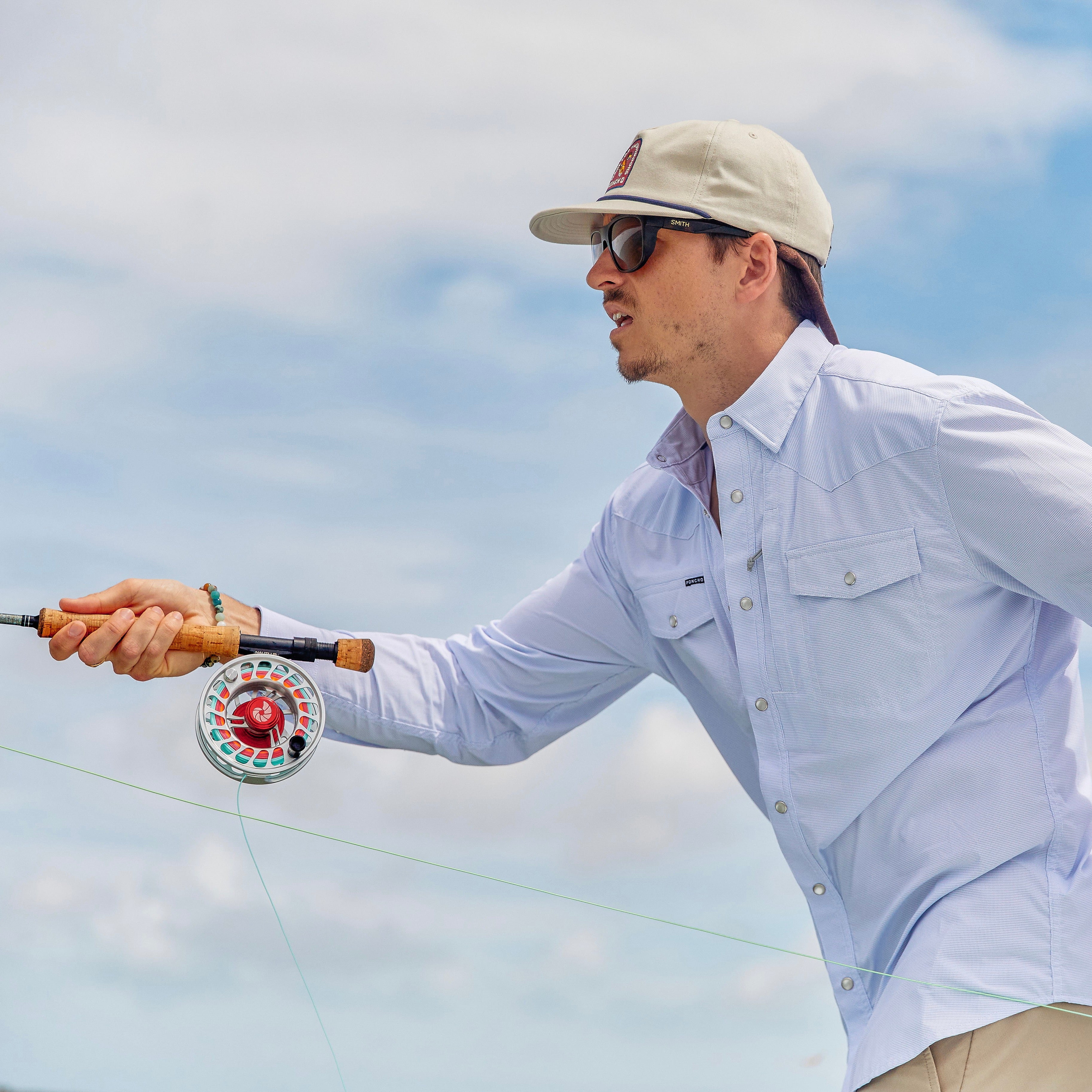 Man casts fly rod while wearing a microcheckered blue and white button down western/performance shirt with pearl snaps