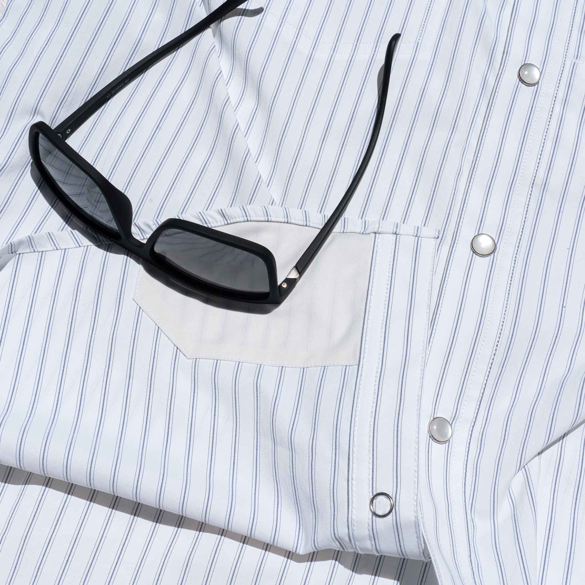 Close up of sunglasses on top of lens cloth of a striped shirt