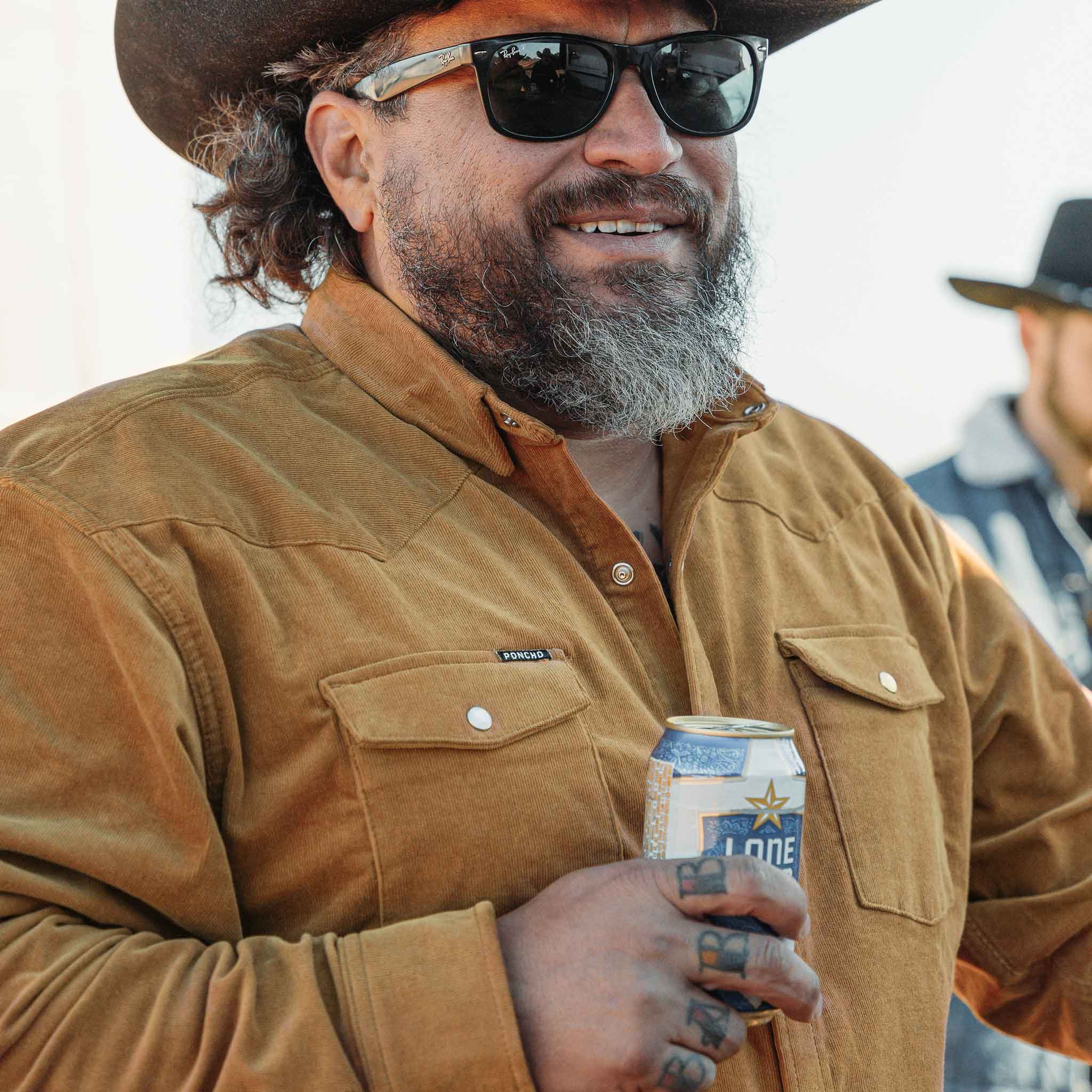 man holding beer and wearing cowboy hat wearing corduroy shirt