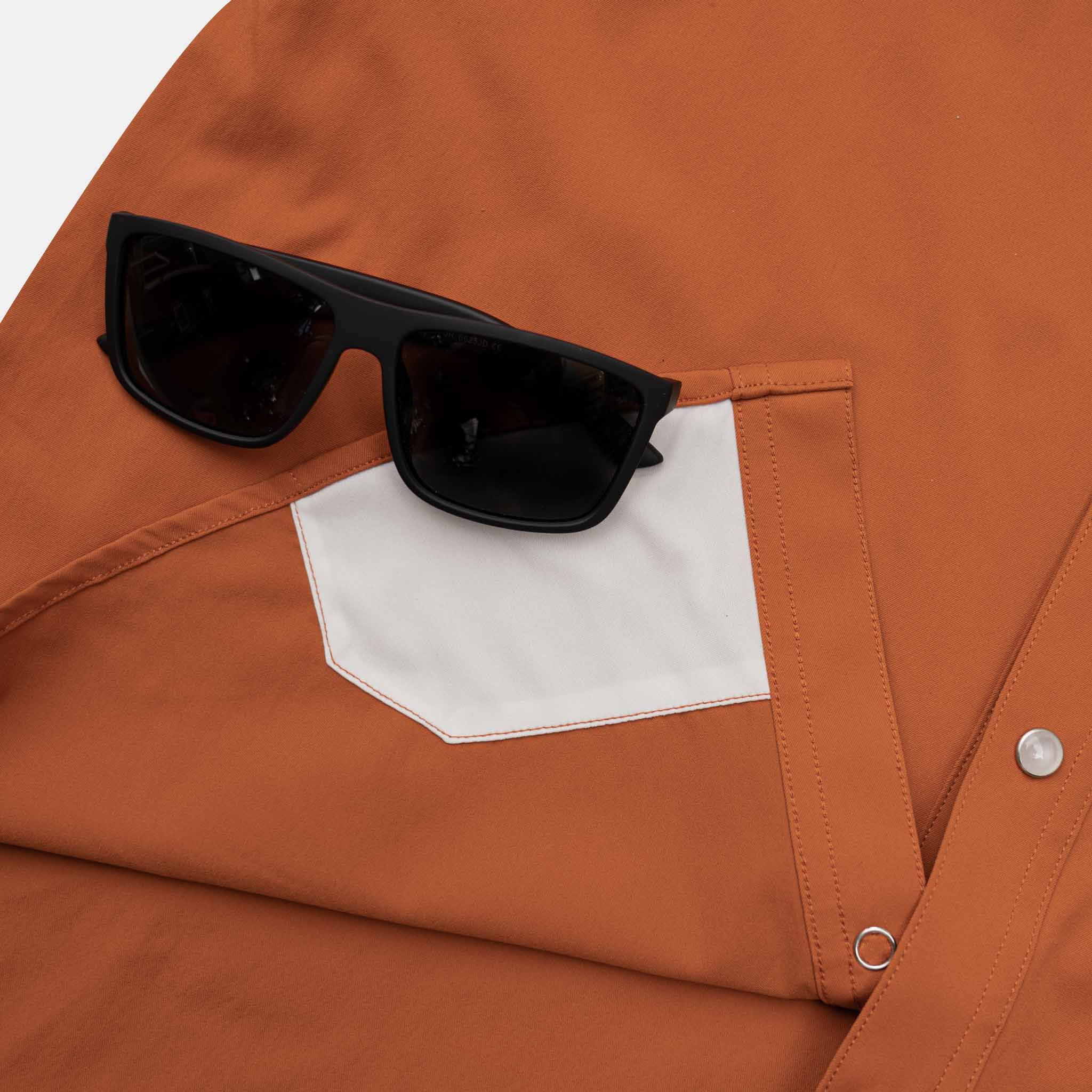 Close up of sunglasses on top of the lens cloth on the burnt orange shirt