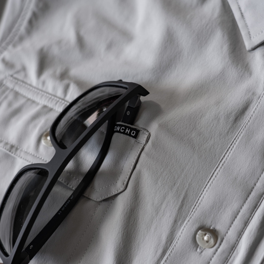 Close up of sunglasses hanging from front chest pocket of grey shirt